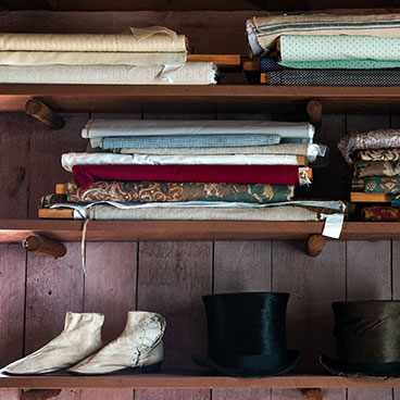 Store shelf filled with fabric bolts, ladies boots and a top hat.